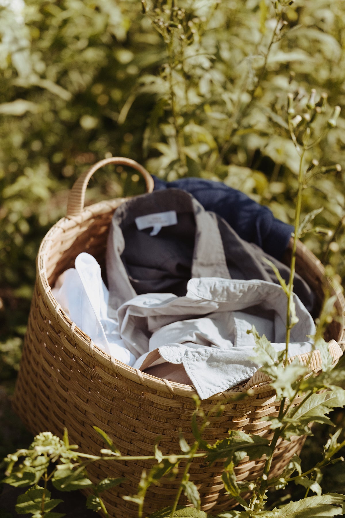 Woven tan basket with two loop handles, filled with folded white and gray linens.