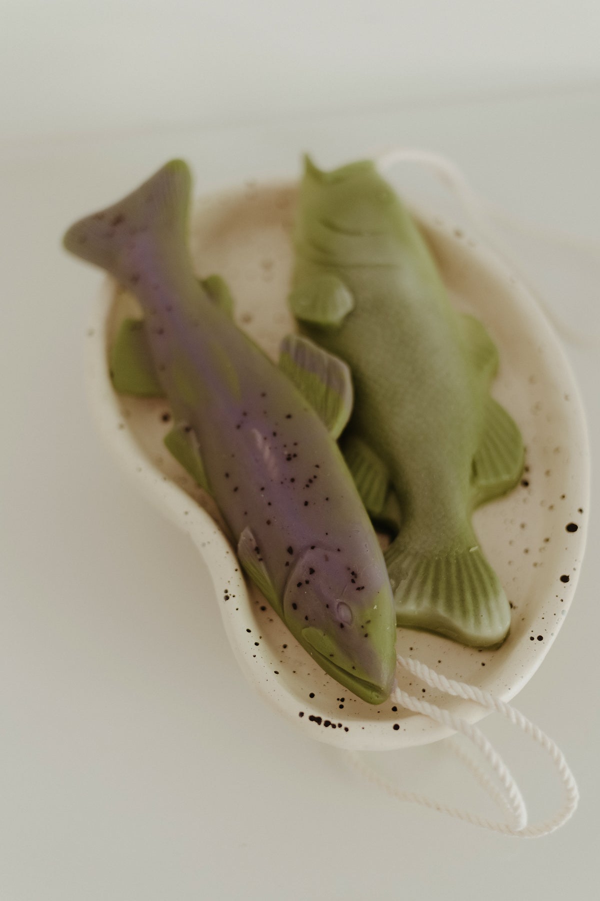 Trout-shaped soap bars with purple and green tones, in white dish