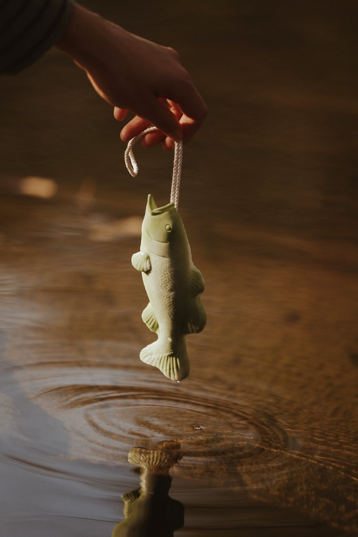 Trout-shaped soap bar on string, held above water by hand