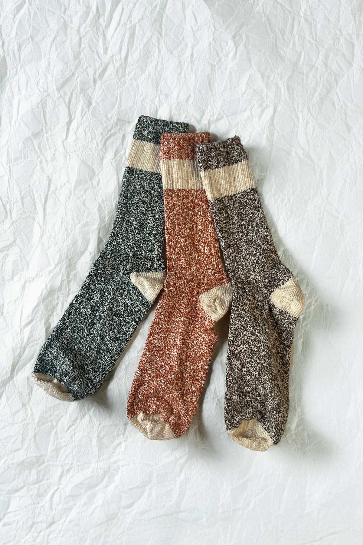 Ragg crew sock bundle laid flat: speckled charcoal, beige, and rust-orange pairs