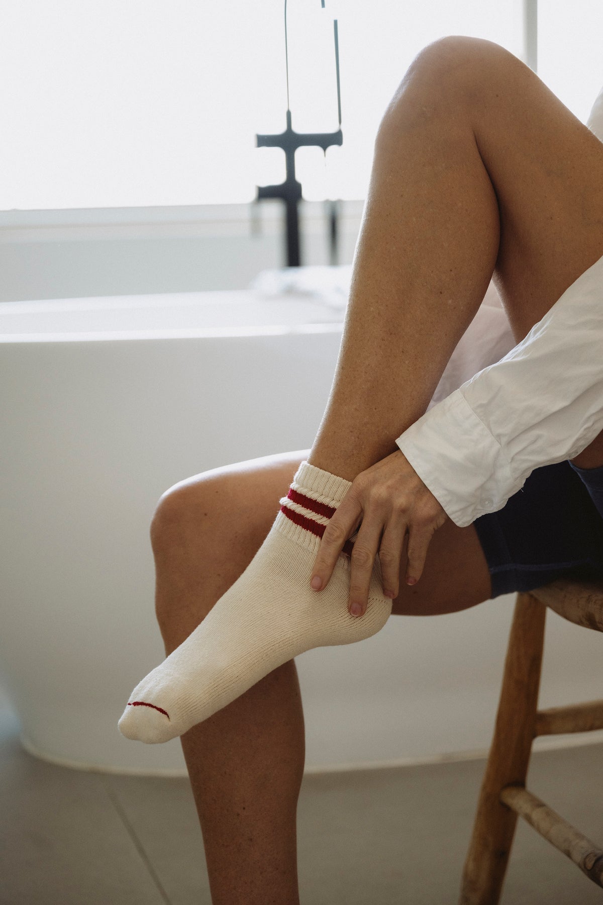 White crew socks with ribbed cuffs and two red stripe bands on a seated leg