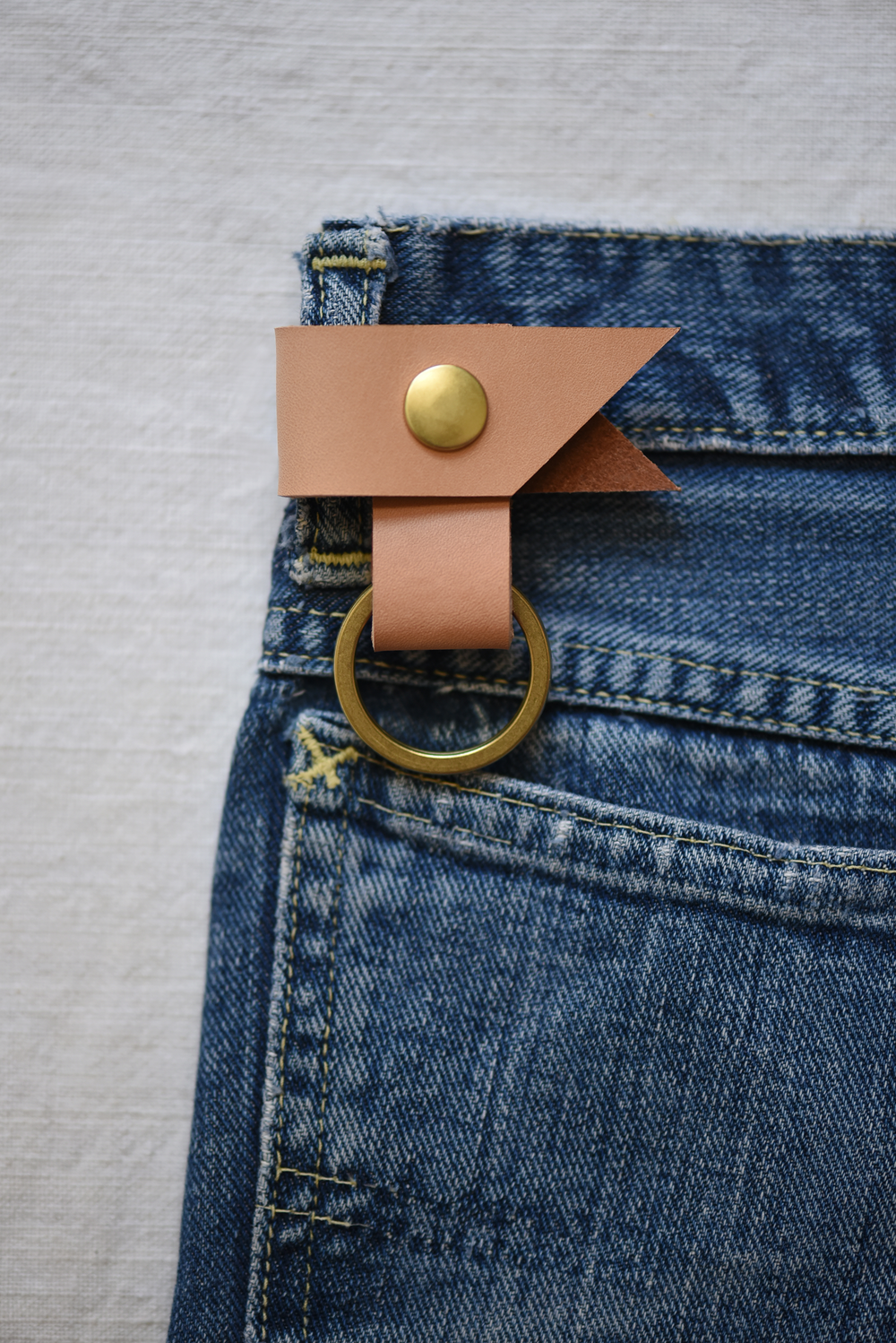 Tan leather keychain with brass snap and ring on denim belt loop